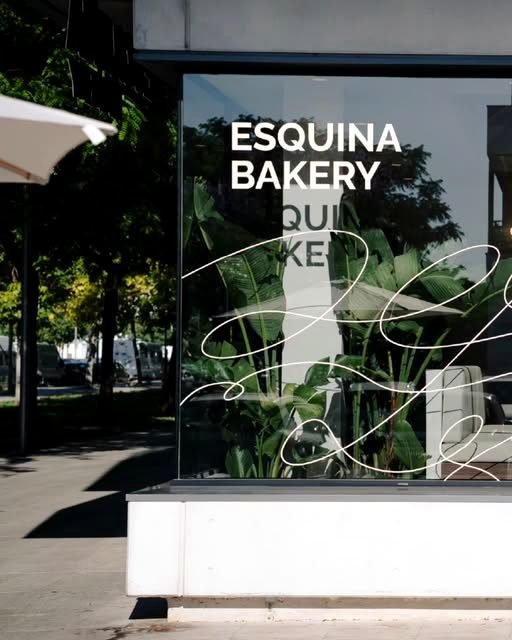 Fachada de Esquina Bakery con el rótulo en el escaparate, la terraza y una sombrilla.