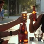 Dos manos brindando con botellas frías en la terraza.