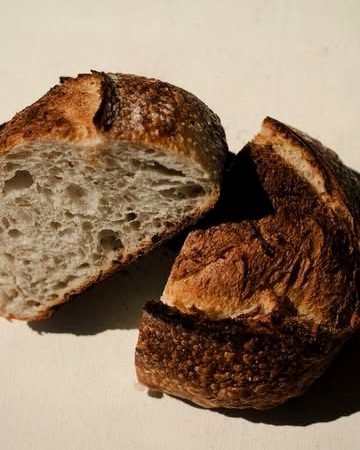 Pan de masa madre partido por la mitad; corteza oscura y miga abierta.