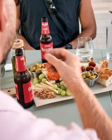 Tabla para compartir con aceitunas, frutos secos, uvas y pan, con bebidas frías, en la terraza.