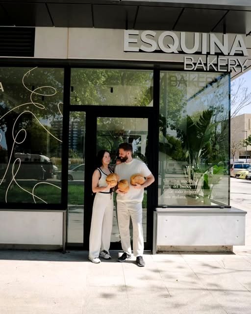 Dos personas del equipo de Esquina Bakery, con pan en las manos, delante de la entrada del local en la Avinguda Mèxic.